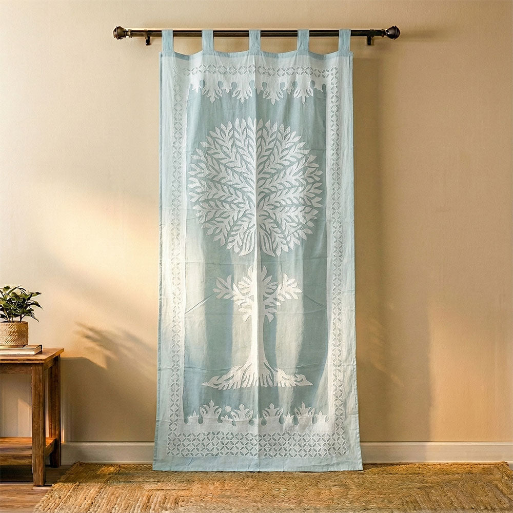 Light blue fabric curtain with white tree design hanging on black rod in cozy room