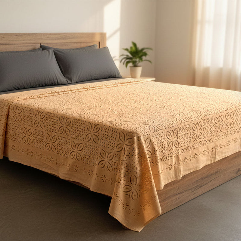 Modern wooden bed with embroidered beige bedspread and two dark gray pillows in sunlit bedroom