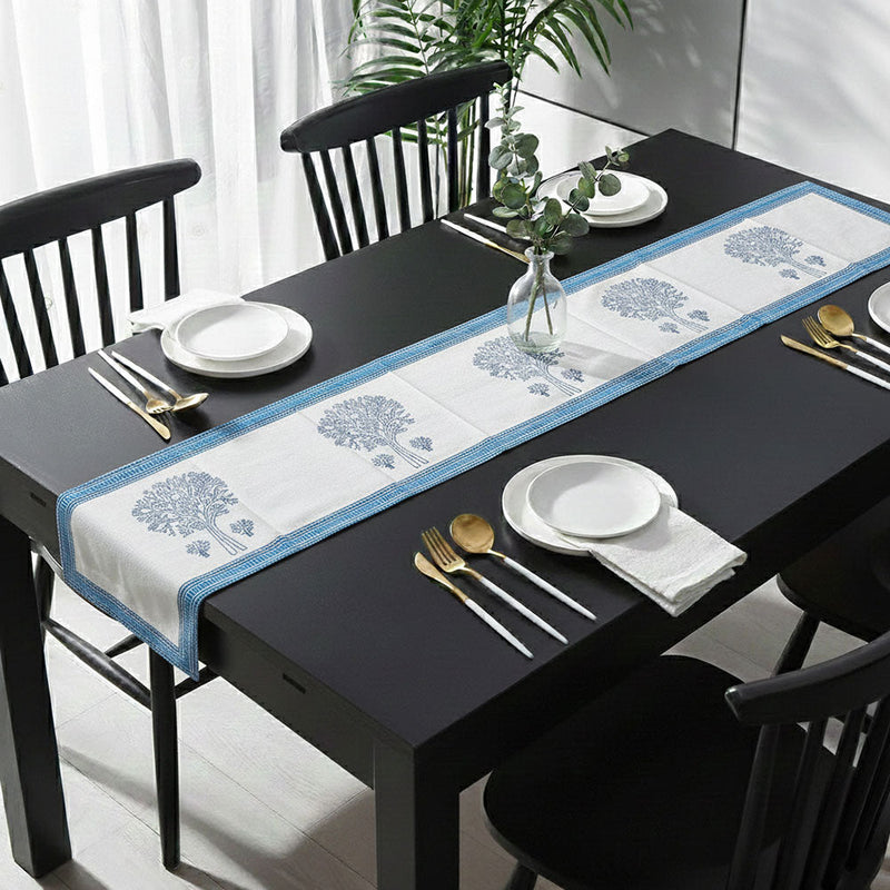 Black dining table with blue and white floral table runner, four place settings, and clear vase with eucalyptus