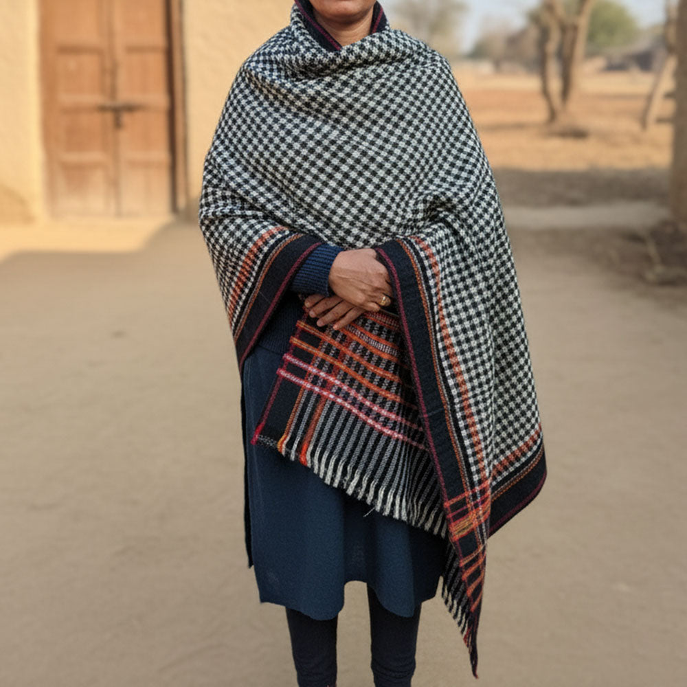 Person wearing a black and white checkered shawl with orange and red plaid border, standing outdoors