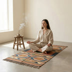 Woman meditating on a patterned rug in a minimalistic room with a wooden stool and plant.