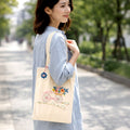 Woman holding a beige tote bag with floral design outdoors