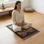 Woman meditating on a colorful rug in a serene room with a wooden desk and meditation cushion.