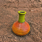 Handmade ceramic vase with green neck and orange body on a textured brown surface