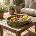 Breakfast tray with croissants, coffee, and fruit on a wooden table outdoors.