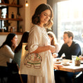 Woman holding a tote bag with an elephant design in a cafe setting