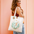 Woman holding a tote bag with a floral design against a pink background