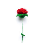 Crocheted red rose with green stem and leaves on a white background