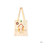 Beige tote bag with embroidered house, flowers, fence, and cloud design, with a round hanging tag