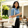 Woman holding a cup and a tote bag with an apple design outdoors.