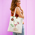 Woman holding a tote bag with a decorative design against a pink background