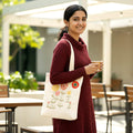 Woman holding a cup and a tote bag with floral design outdoors