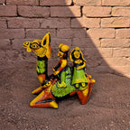 Colorful figurine of a camel with two people against a brick wall.