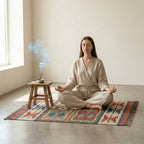 Woman meditating on a colorful rug with a wooden stool and plant.