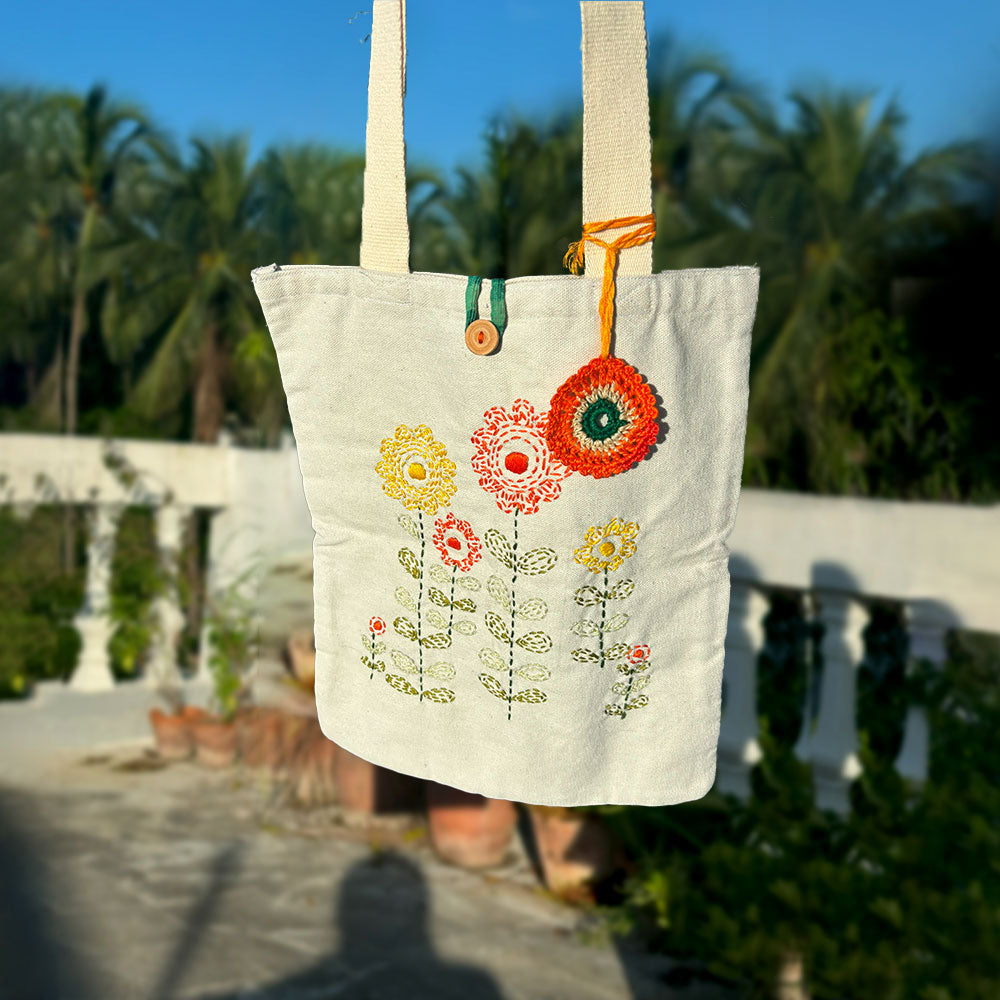 Beige fabric tote bag with embroidered colorful flowers and circular orange ornament hanging outdoors