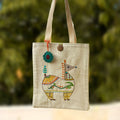 Tote bag with colorful embroidered design of a creature on a blurred green background