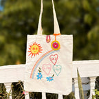 Beige canvas tote bag with colorful embroidery of sun, rainbow, flowers, and hearts with text sky is the limit
