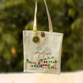 Canvas tote bag with embroidered design of a village scene against a blurred green background