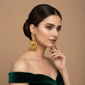 Woman wearing golden earrings with a green top against a beige background