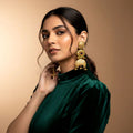 Woman wearing gold earrings against a beige background