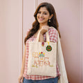 Woman holding a tote bag with floral design against a pink background