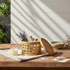 Decorative basket with lavender on a wooden table with a candle and plants in the background.