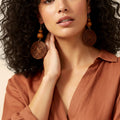 Woman wearing large wooden earrings with a neutral background