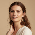 Woman wearing large, round earrings against a beige background