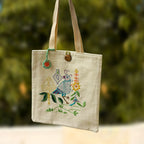 Tote bag with embroidered design of a robot and flowers against a blurred green background