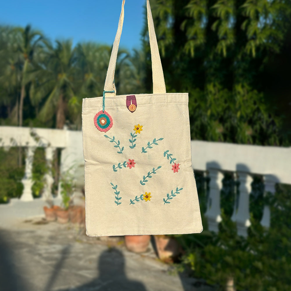 Beige cotton tote bag with colorful floral embroidery hanging outdoors in sunlight
