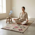 Woman meditating on a patterned rug with a small wooden stool and diffuser in the background.