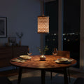 Dining table set with plates, glasses, and a vase under a hanging lamp in a dimly lit room.