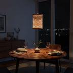 Dining table set with plates, glasses, and a vase under a hanging lamp in a dimly lit room.