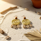 Pair of earrings with shell accents on a sandy surface with driftwood and shells.