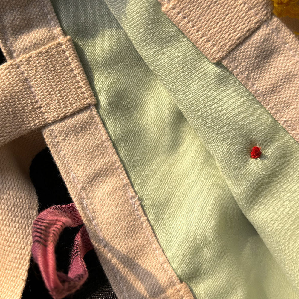 Close-up of beige canvas straps and light green fabric with a small red thread knot detail