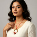 Woman wearing a necklace with a red cord and floral pendant against a gray background