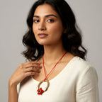 Woman wearing a necklace with a red cord and floral pendant against a gray background