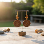 Pair of bronze earrings on a stand with natural elements in the background