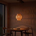 Woven pendant light hanging above a wooden table with chairs in a dimly lit room.
