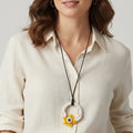 Woman wearing a necklace with a yellow flower pendant on a plain background