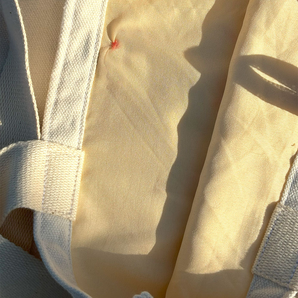 Close-up of cream-colored fabric bag interior with textured white handles and red stitching detail