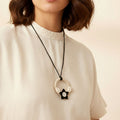 Person wearing a necklace with a black and white pendant on a plain background