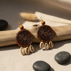 Pair of brown spiral earrings with cowrie shell pendants on a natural setting with stones and driftwood.
