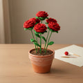 Knitted red roses in a terracotta pot on a wooden surface with a neutral background