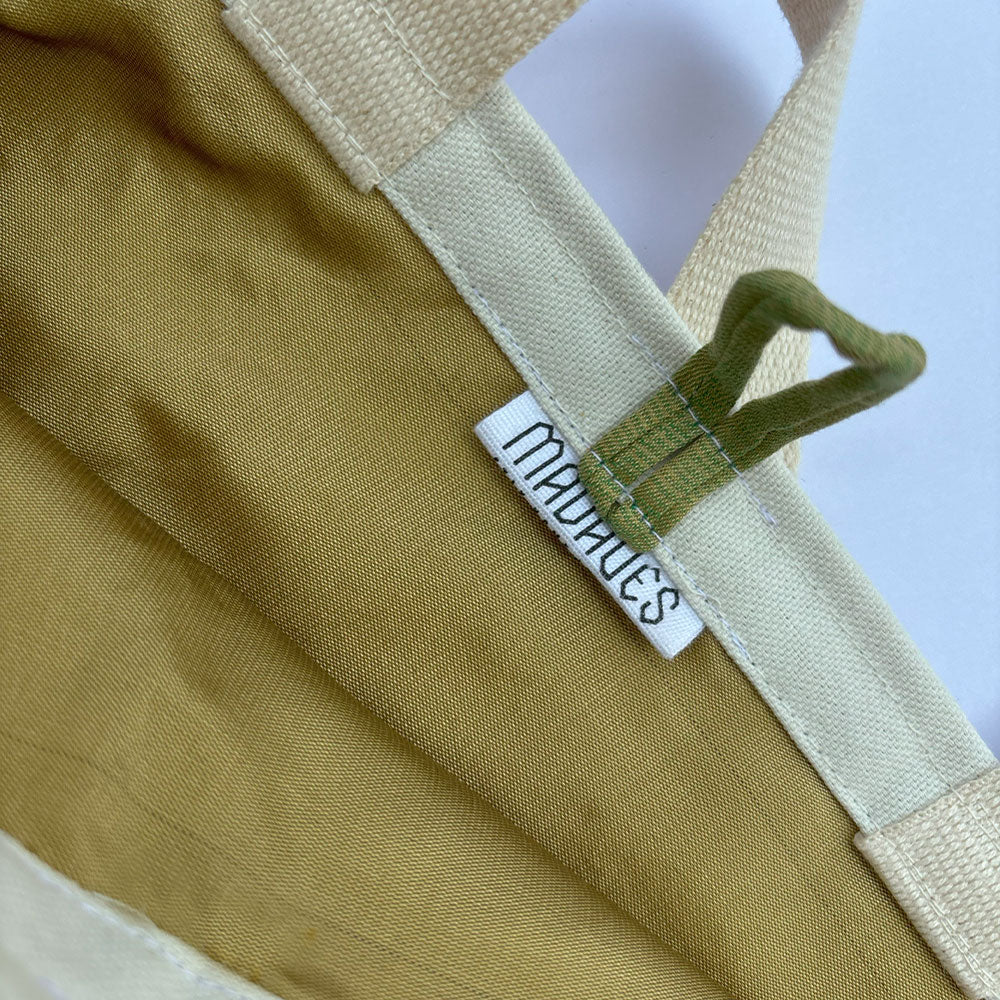 Close-up of beige cotton bag with green inner strap and stitched tag labeled 'MALVIES'