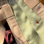 Close-up of beige canvas strap and light green fabric with red stitching detail, showing texture and colors