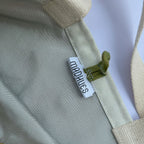 Close-up of a beige bag with a 'MADHUES' label on a light gray background