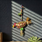 Decorative Bird  ornament with colorful beads against a dark wall with sunlight casting shadows.