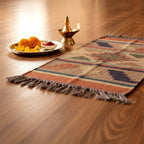 Decorative rug with fringe on a wooden floor, accompanied by a small altar with flowers and a lamp.