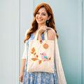 Woman holding a tote bag with a bird design against a light blue background